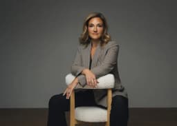 Stephanie Gilezan in houndstooth blazer, seated on bouclé chair